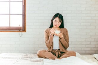ベッドの上でヨーグルトを食べようとしている女性