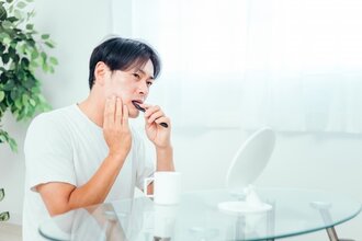 歯磨きをしながら歯を気にしている男性